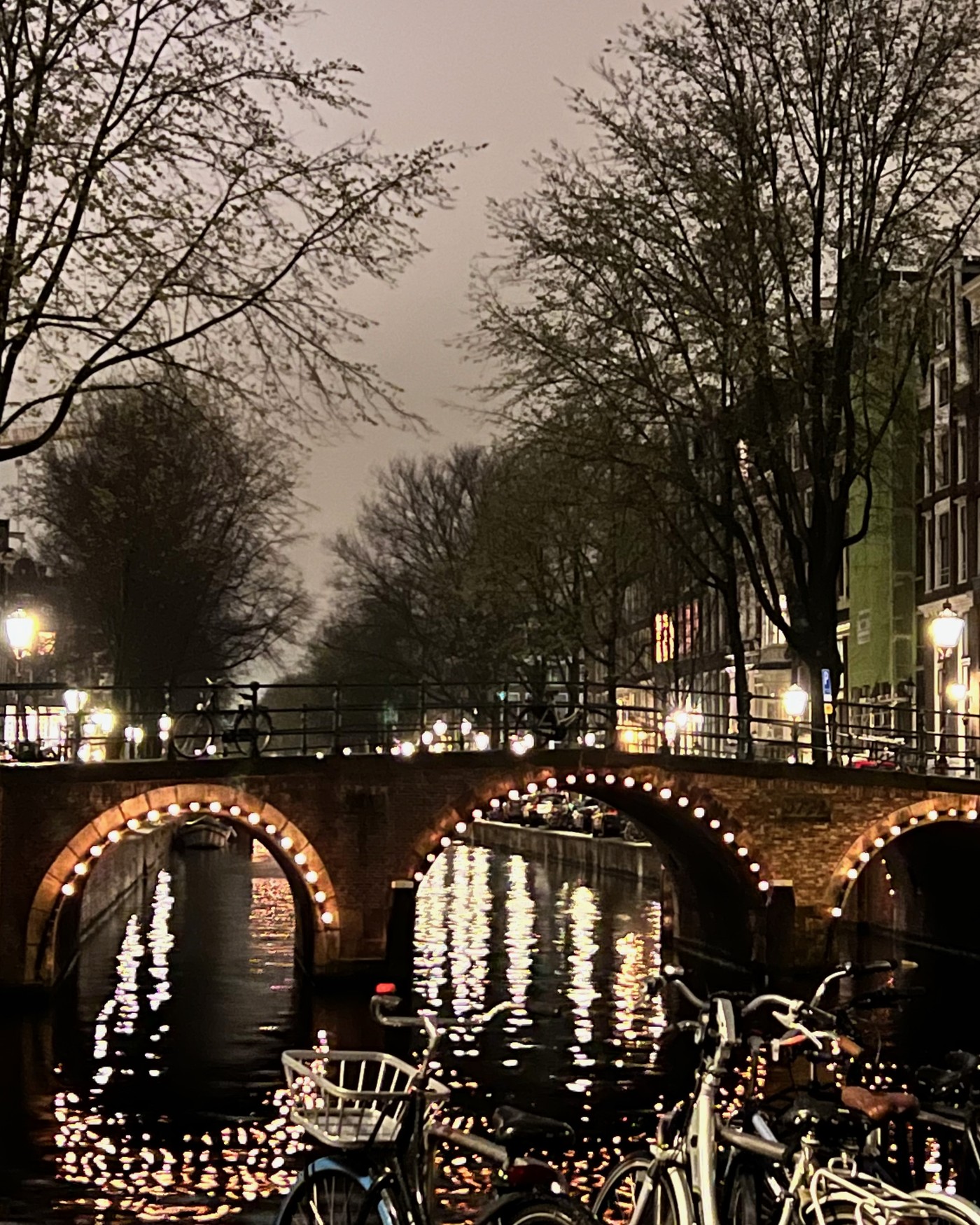 Lit arches of a canal bridge in Amsterdam at dusk with bicycles along the rail