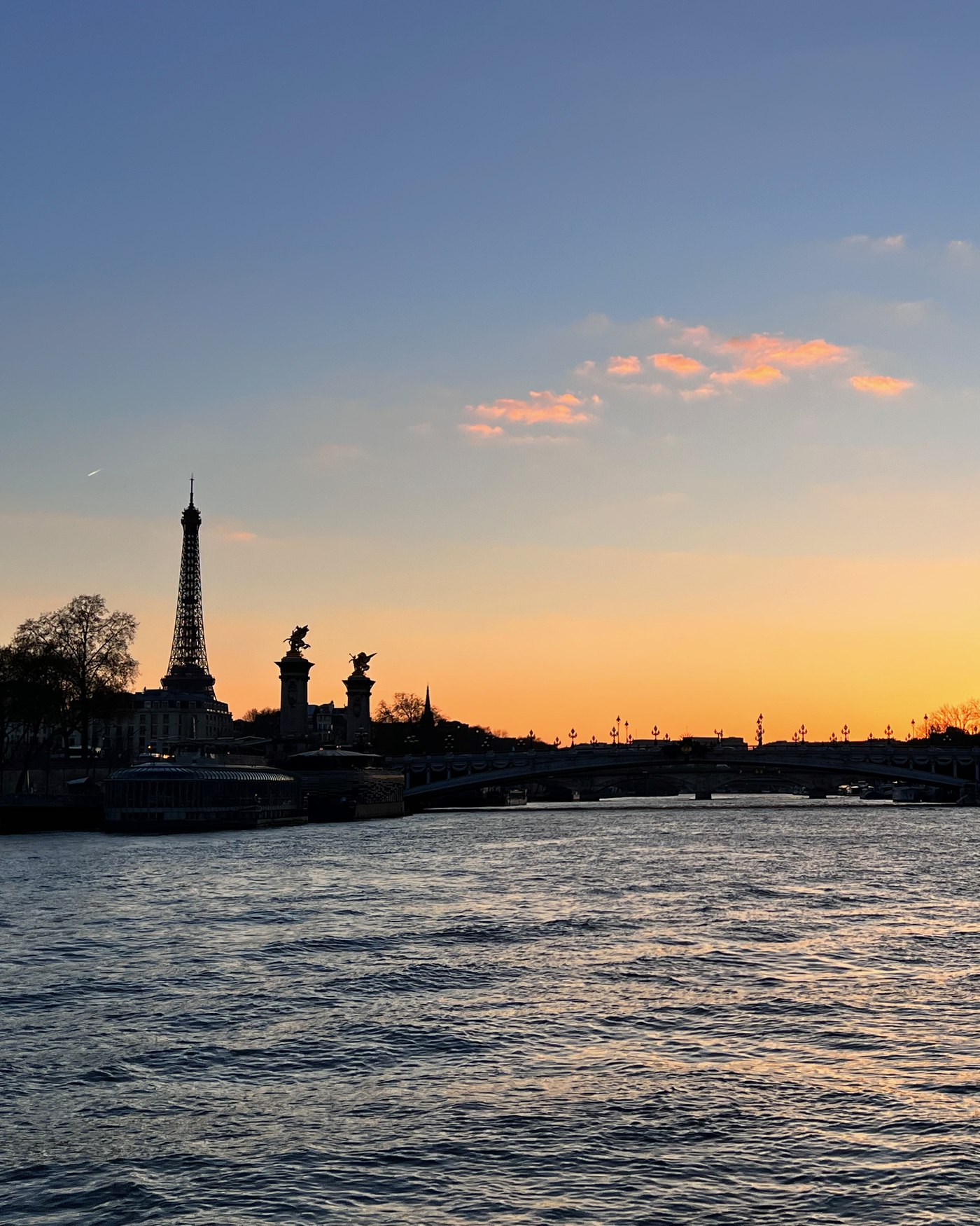 Pont Alexandre III and the Eiffel Tower silhouetted against a gold sunset over the Seine